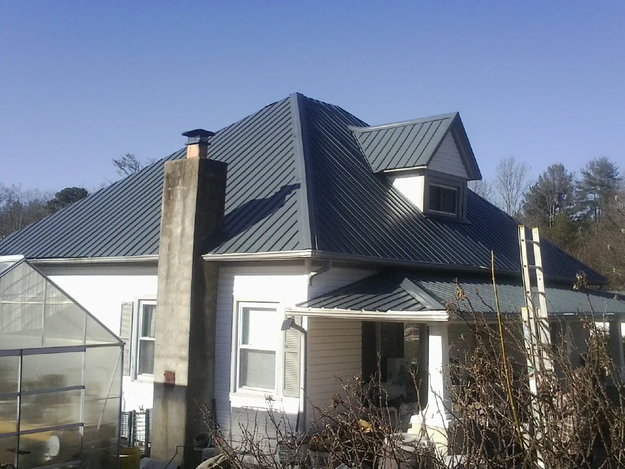 Dark blue standing seam metal roof on a white farmhouse with dormer — Slate & Tile Roof Repair by Roofing Brothers in Rowe