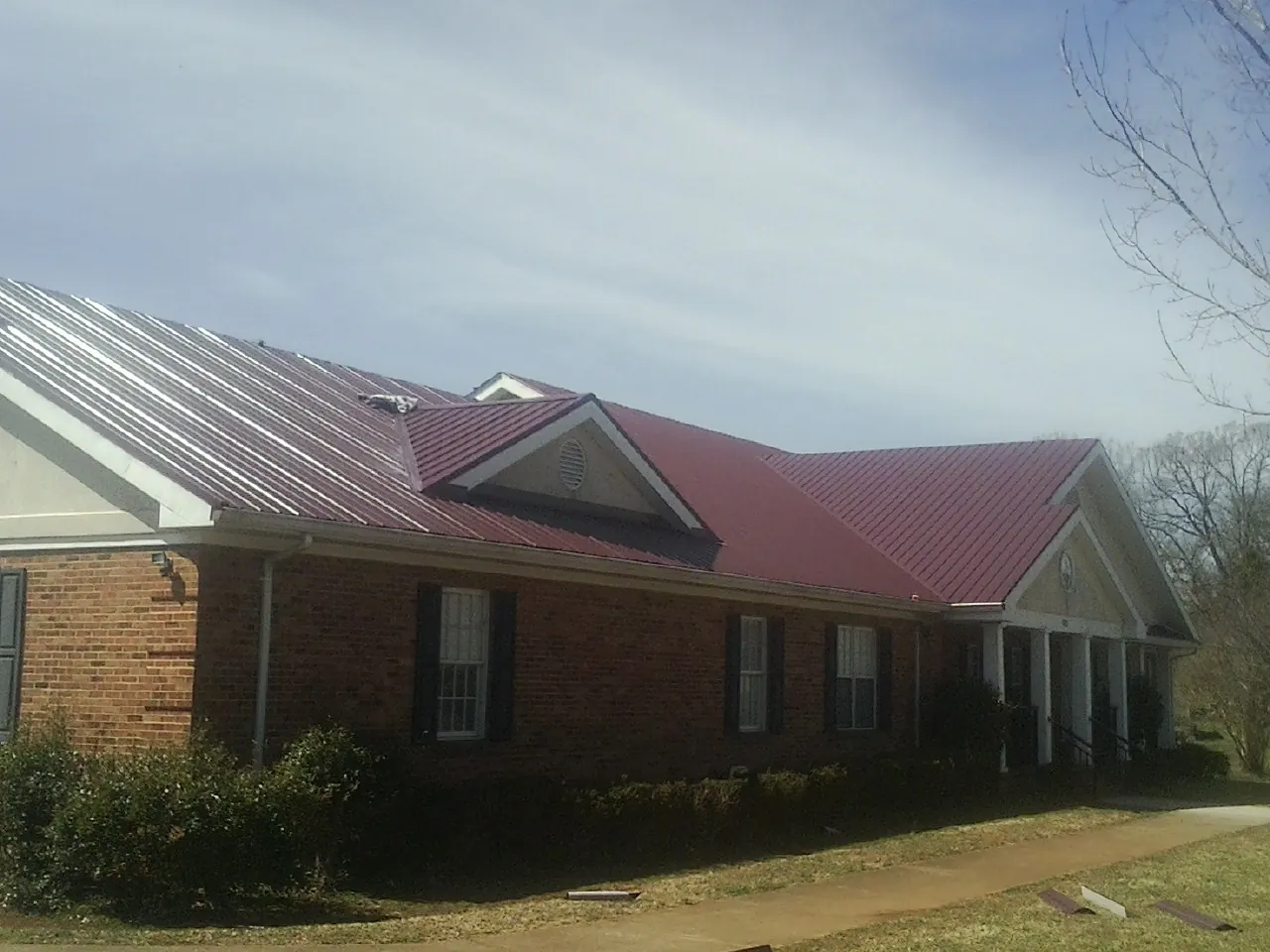 Red metal roof with gabled entries on a long brick building, from a Hail Damage Roof Repair job in Rowe