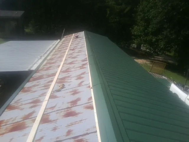 Old rusted panels beside newly installed green metal roofing — Wind Damage Roof Repair by Roofing Brothers in Rowe
