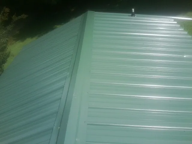 New green metal panels meeting at the ridge of a roof — Flat Roof Repair work by our crew in Rowe