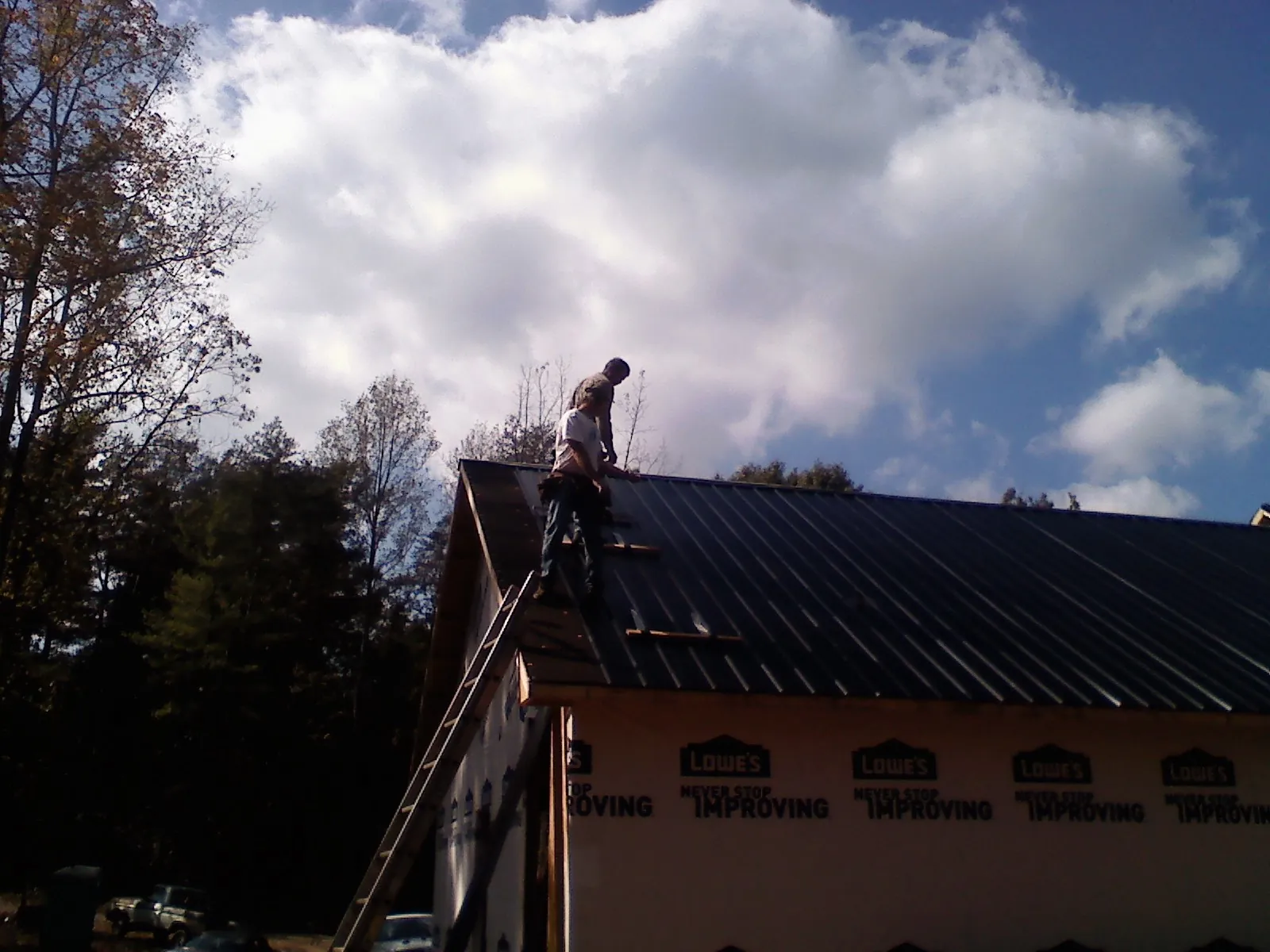 Roofer fastening dark metal panels high against a cloudy sky, from a Roof Inspection job in Rowe
