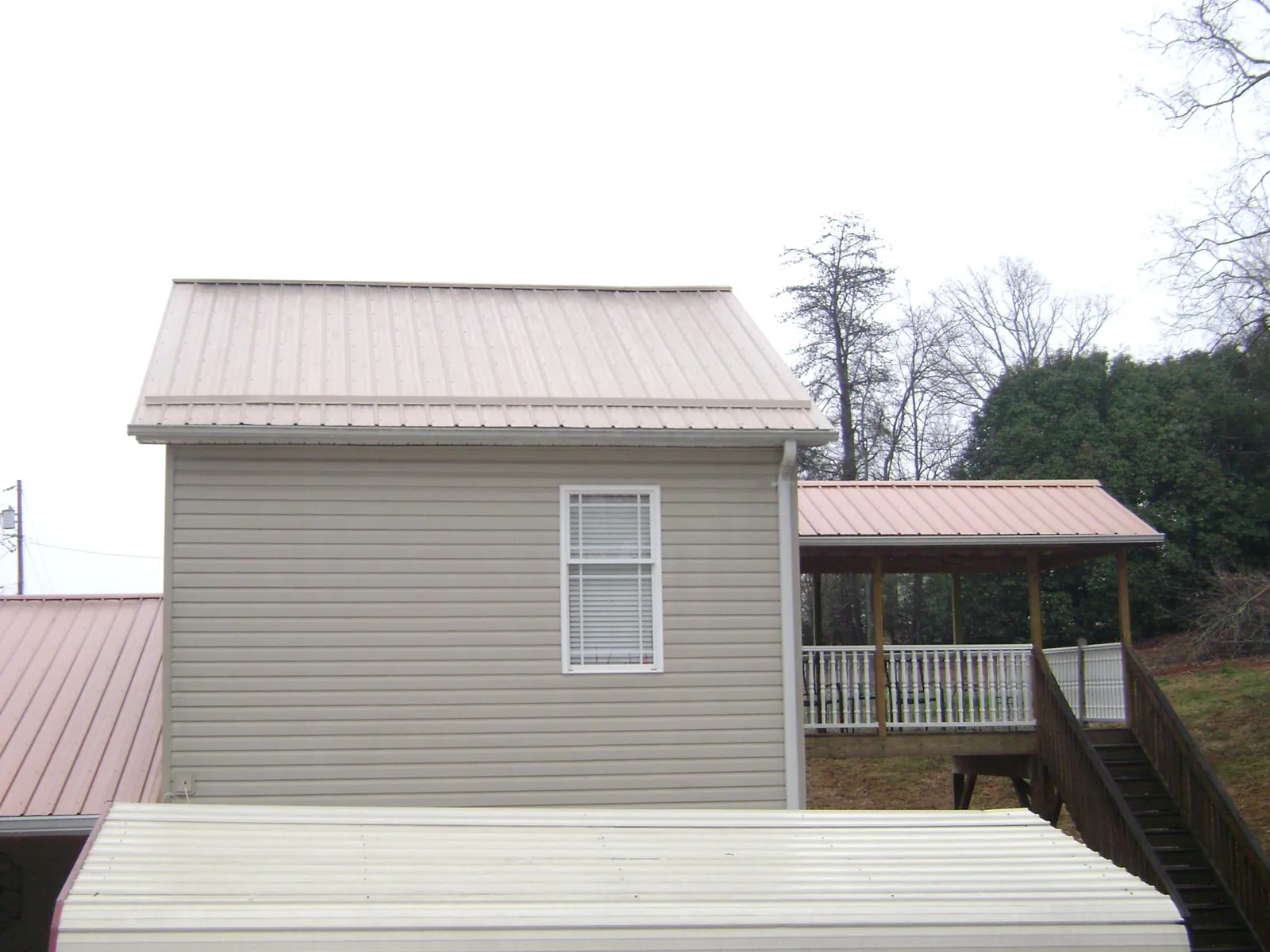 Tan metal roofs on a two story addition and attached porch, from a Roof Replacement job in Rowe