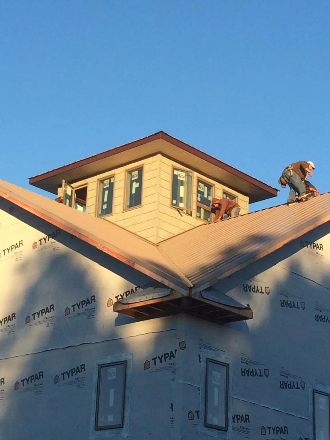 Roofers working around a rooftop cupola on a new metal roof at sunset — Roof Waterproofing in Rowe by Roofing Brothers